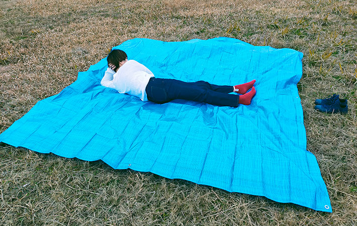ダイソー　レジャーシート約４.５畳サイズ（ブルー、約２７０×２７０cm）シートを広げその上に大人が寝転がる様子
