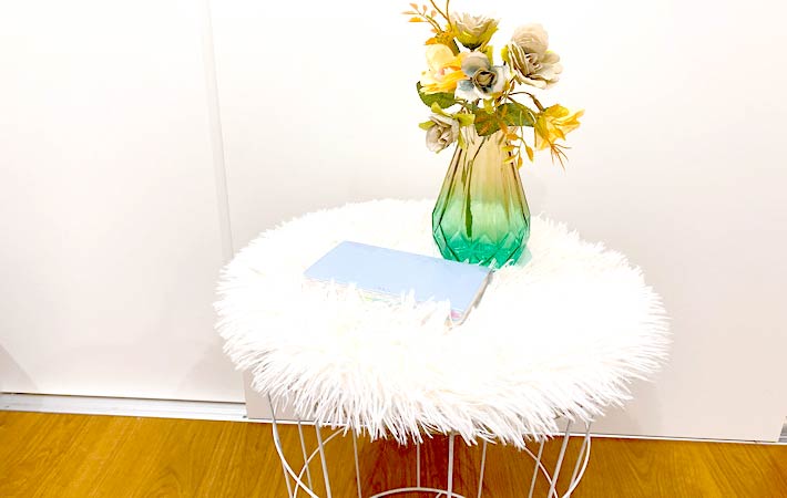 『サイドテーブル（ラウンド、ナチュラル）』のテーブルの上にクッションを敷き、花瓶や本などインテリア小物を置いてアレンジした様子
