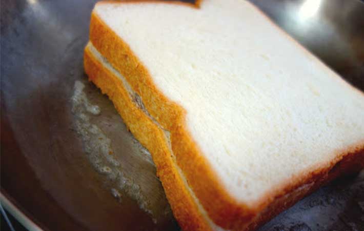 フライパンで焼いている『「ブレンディ®」スティック カフェオレ』とバターがのっている食パンの上からもう１枚食パンをのせた写真