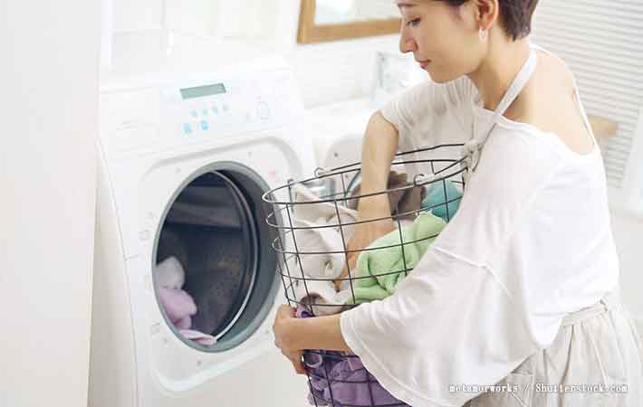 洗濯機の前で女性がランドリーバスケットを持っている画像