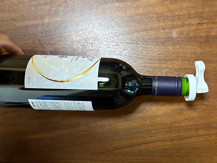 ダイソーの『何度でも使えるボトルキャップ』をワインボトルの口に装着しボトルを」横向きに置いている写真