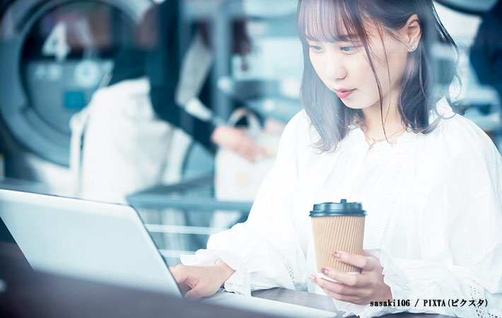 コーヒーを片手にパソコン操作をする女性の写真