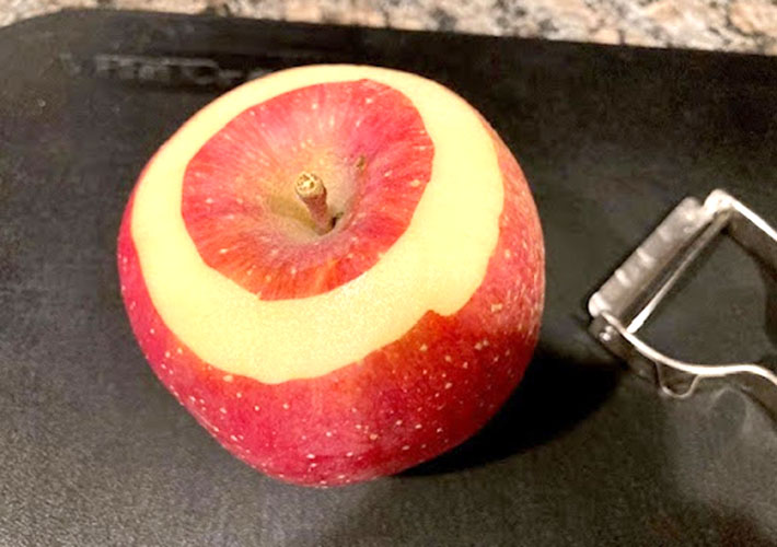 ピーラーでリンゴの上の部分を1周皮をむいた状態の写真