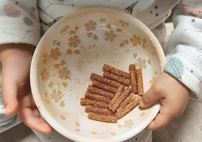子供が手に持っている皿に入っているマカロニでできた『かりんとう』の写真
