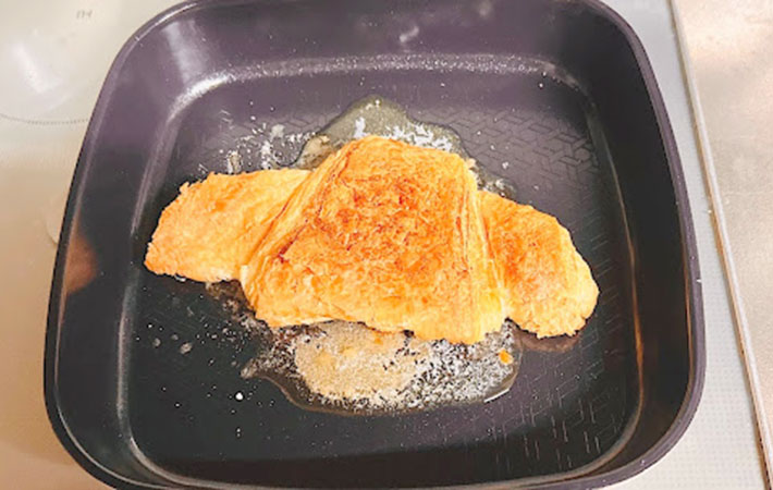 フライパンにバターと砂糖を入れクロワッサンを上から焼く様子の写真