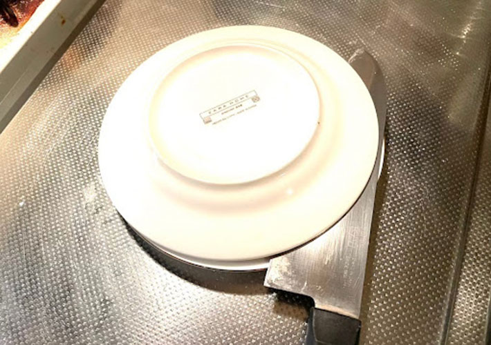 プチトマトを２枚の皿で挟み皿と皿の間から包丁を入れカットしている様子の写真
