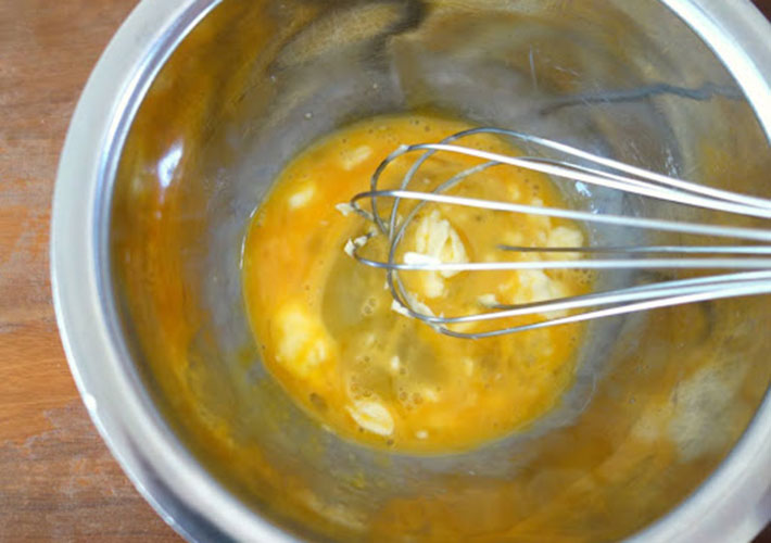 ボウルに卵を入れ溶かしバターを加えて混ぜている写真