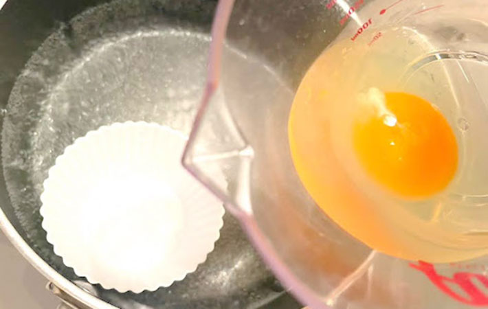 沸騰したお湯が入ったポットの中にシリコンカップを浮かばせ生卵をカップに入れる写真