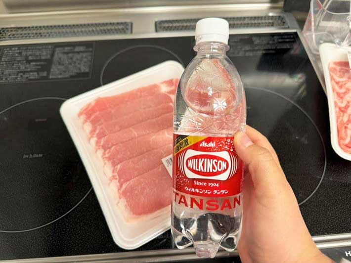 豚肉が置かれたキッチンで炭酸水を手に取った写真