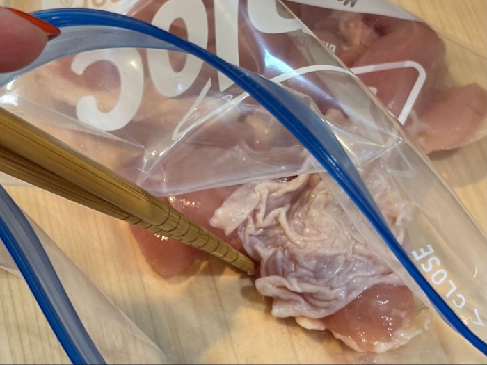 箸でジッパーつきのポリエチレン袋に入れている鶏肉の写真