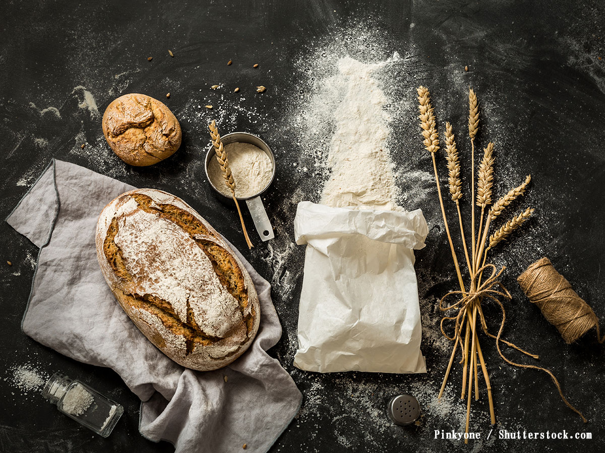 白い紙の袋から小麦粉がこぼれ計量カップとパンの写真