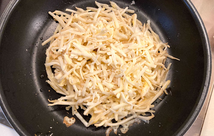 フライパンにサラダ油を入れてもやしのチヂミにチーズを乗せ焼いている写真