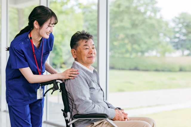 病院・施設で車椅子に乗る高齢者と看護師の画像