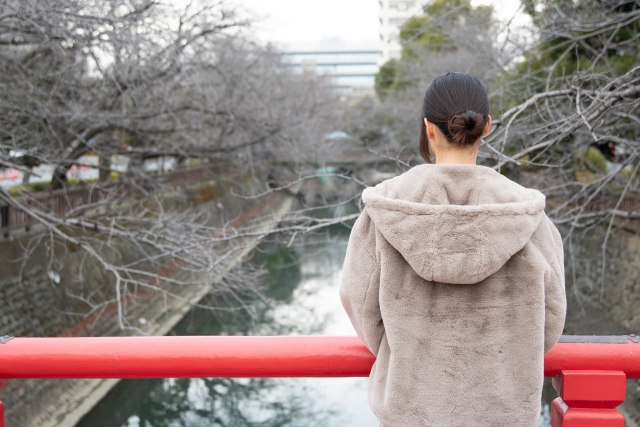 冬の川を見つめる女性の後ろ姿