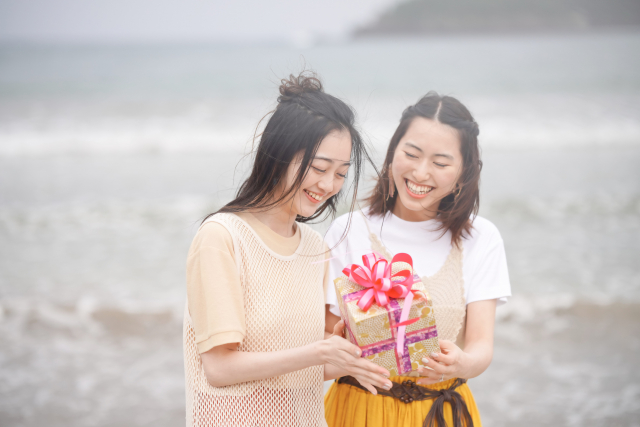 波打ち際でプレゼントを持つ若い女性2人の画像