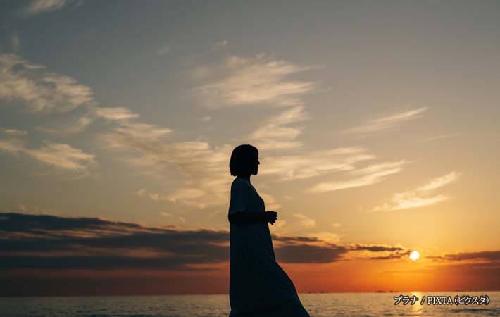 夕焼けの浜辺を歩く女性の写真