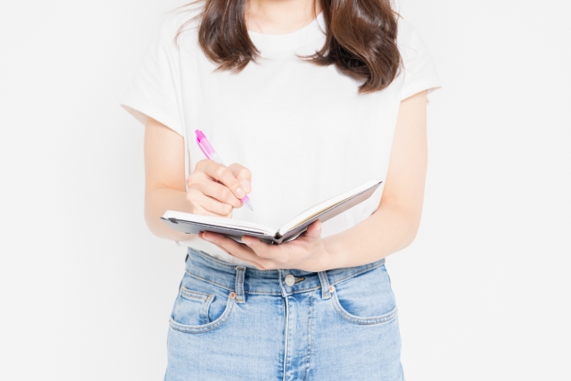 ノートにメモを書くTシャツを着た若い女性の画像