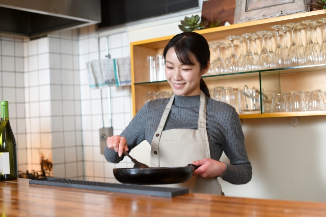 飲食店の厨房で調理をする笑顔の若い女性の画像