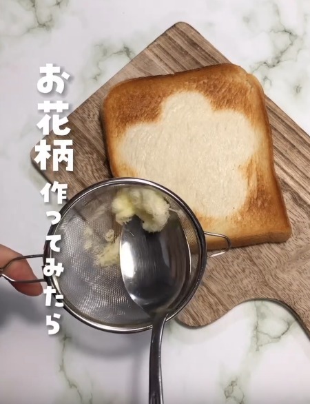 まな板の上に置かれたトーストと茶こしの中のバターをスプーンですくう様子
