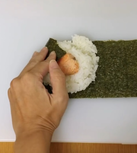 後は海苔で包んでいくだけでOKです。まずは海苔の左上部分をつかみ、斜め下方向へと包み込みましょう。