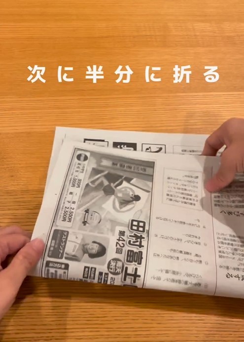 ２枚の新聞紙をそのまま重ねて、縦長になるように置いたら、さらに半分に折りましょう。