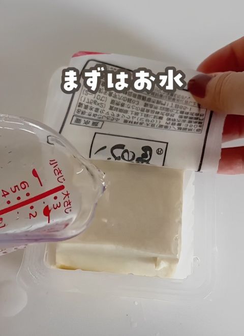 豆腐のパックに計量カップで水を入れる様子