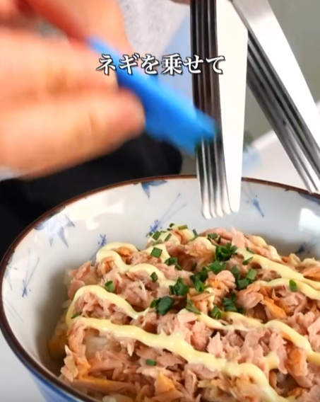 ツナ丼の上にネギをのせる様子