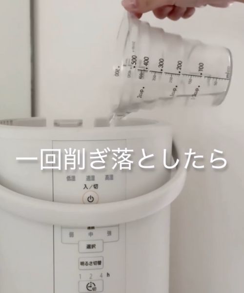 加湿器のタンクに目盛りの付いたカップで水を入れる様子