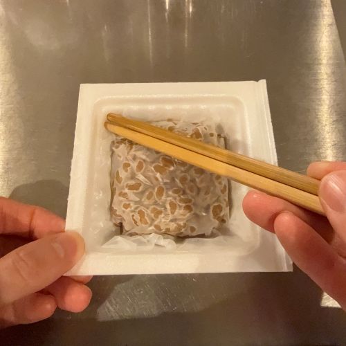 納豆を開けてフィルムのかかっている内側面の１箇所に内側から箸で穴を開けた様子