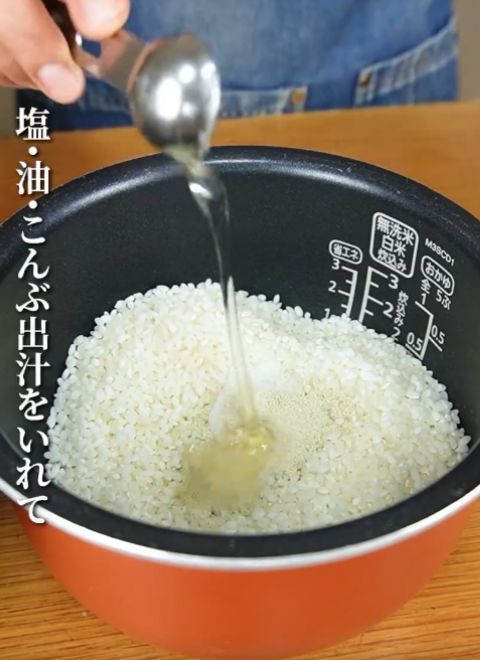 米を入れた炊飯釜に計量スプーンで調味料を入れる様子