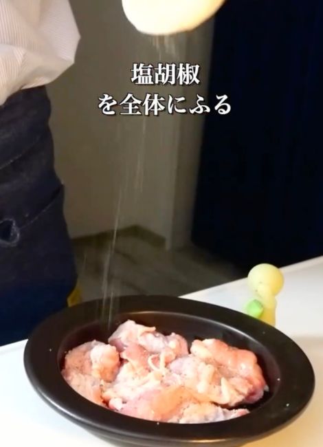 高い位置から鶏肉に塩こしょうを振りかける様子