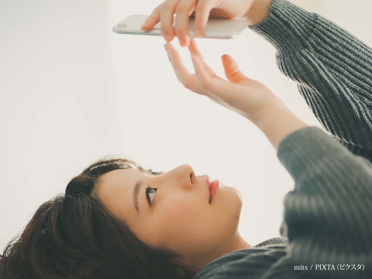 寝ながらスマホをする女性の写真