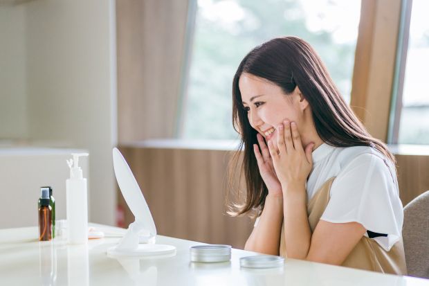 スキンケアをしながら鏡に笑顔を向ける女性の写真