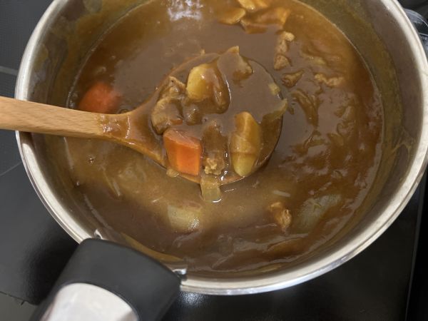 鍋に入ったカレーをおたまで混ぜている写真