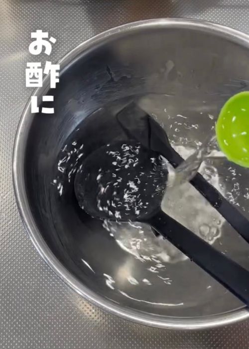 熱湯を入れたボウルに酢を計量スプーンで入れる様子