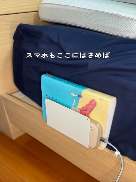 ベッドとマットレスの間に挟んだブックエンドに本と充電中のスマートフォンを収納した様子