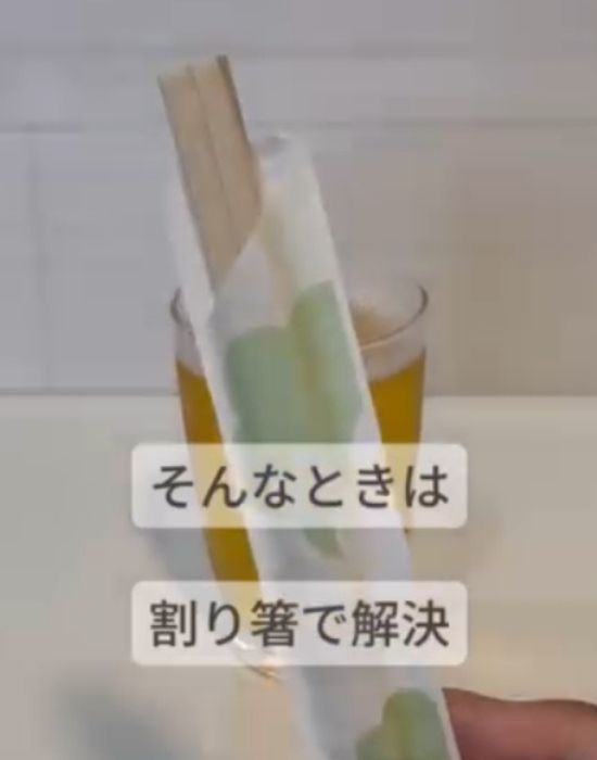 グラスに注いだビールを背景に袋に入った割り箸を持っている様子の写真