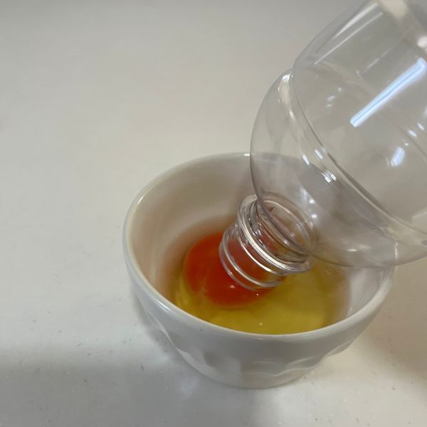 空のペットボトルの口を卵黄に近づける様子