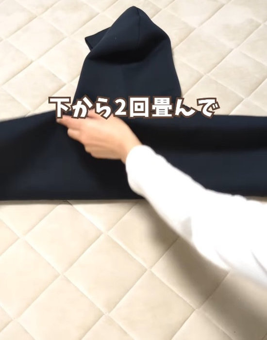 背中側を上にして広げたパーカーの胴の部分を下から折り畳む様子