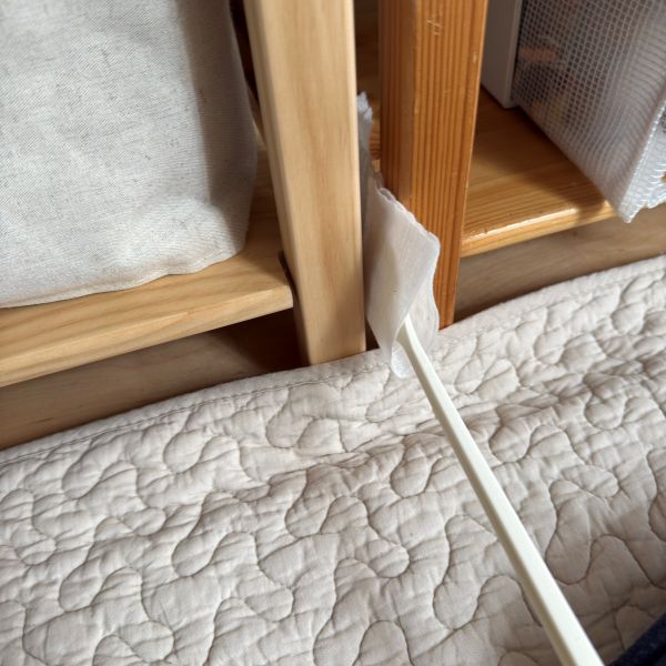 掃除用シートを付けたハンディワイパーで家具の隙間を掃除する様子