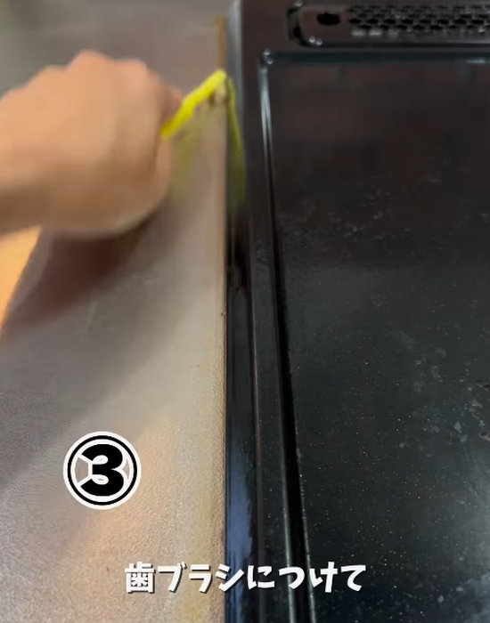 コンロのフチのすき間を歯ブラシで掃除する様子
