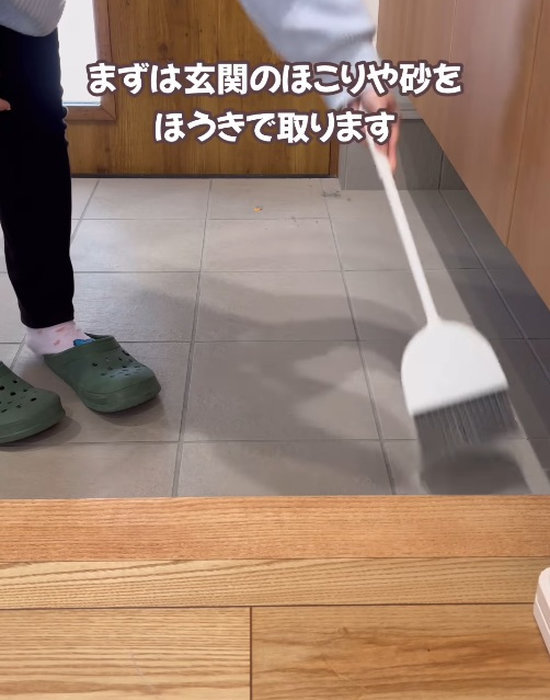 玄関をほうきで掃除をしている人