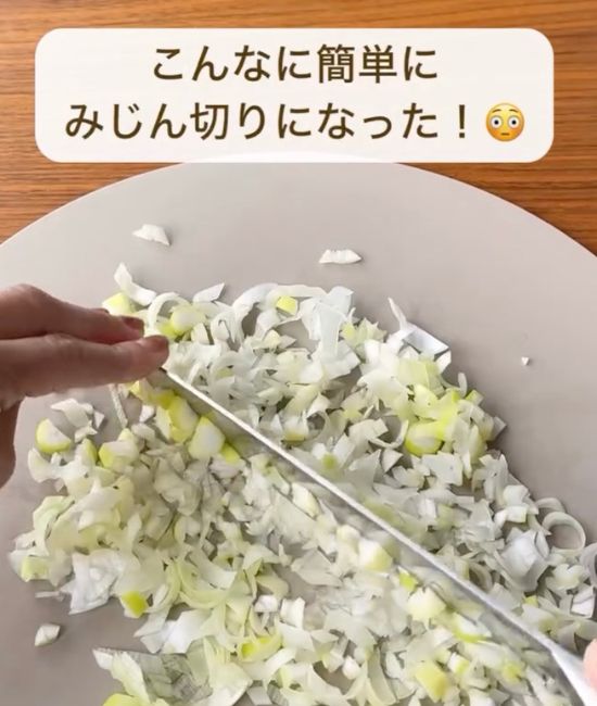 包丁を持っていない手で刃先を押さえながら長ネギを細かくみじん切りする様子