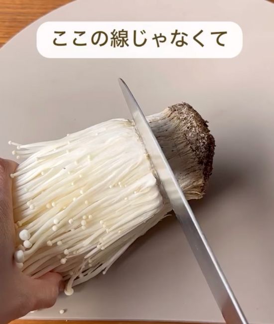 エノキの根元のくびれ部分に包丁を入れる様子