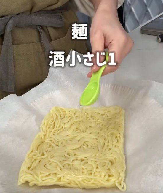 クッキングシートを敷いた皿の上に焼きそばの麺を置いて上から料理酒をかける様子