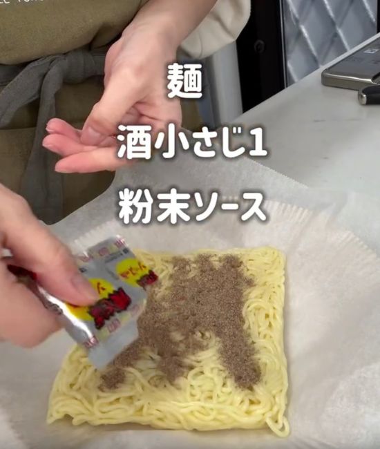 クッキングシートを敷いた皿に置いた焼きそばの上に粉末ソースをかける様子