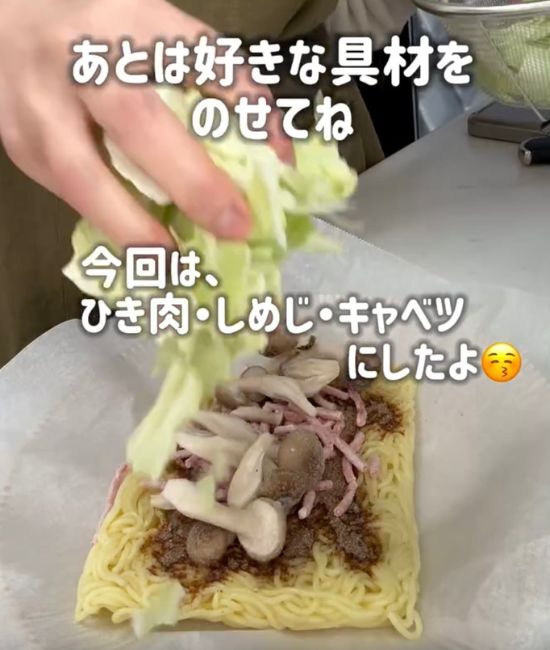 粉末ソースをかけた焼きそばの麺の上に具材をのせる様子