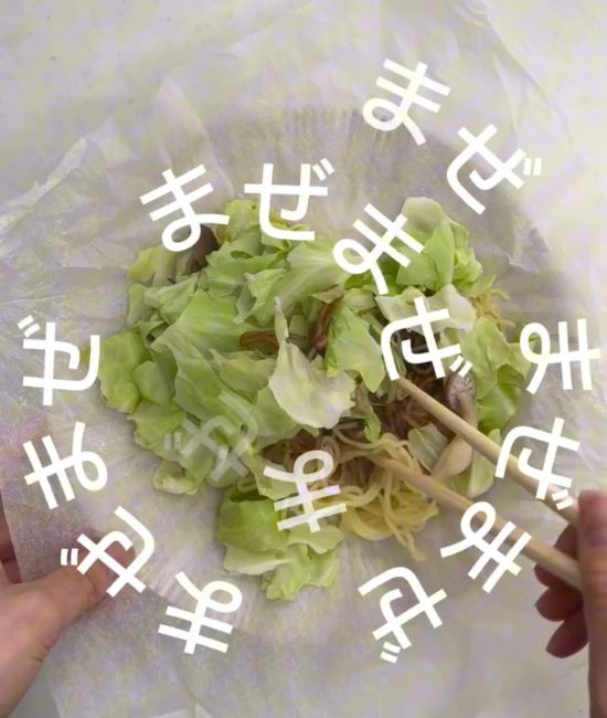 クッキングシートの口を開けて焼きそばの麺と具材を箸で混ぜる様子