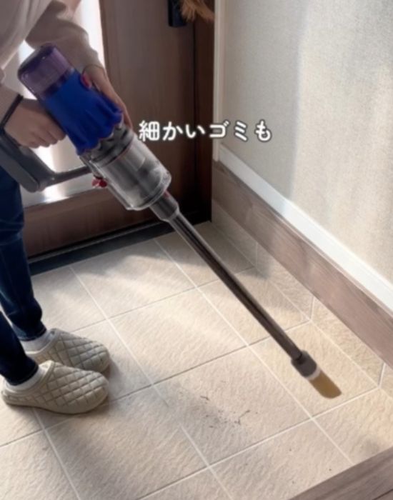 トイレットペーパーの芯を付けた掃除機で玄関のゴミを吸い取ろうとしている様子