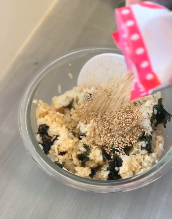ワカメと調味料を混ぜたご飯に白ゴマをかける様子